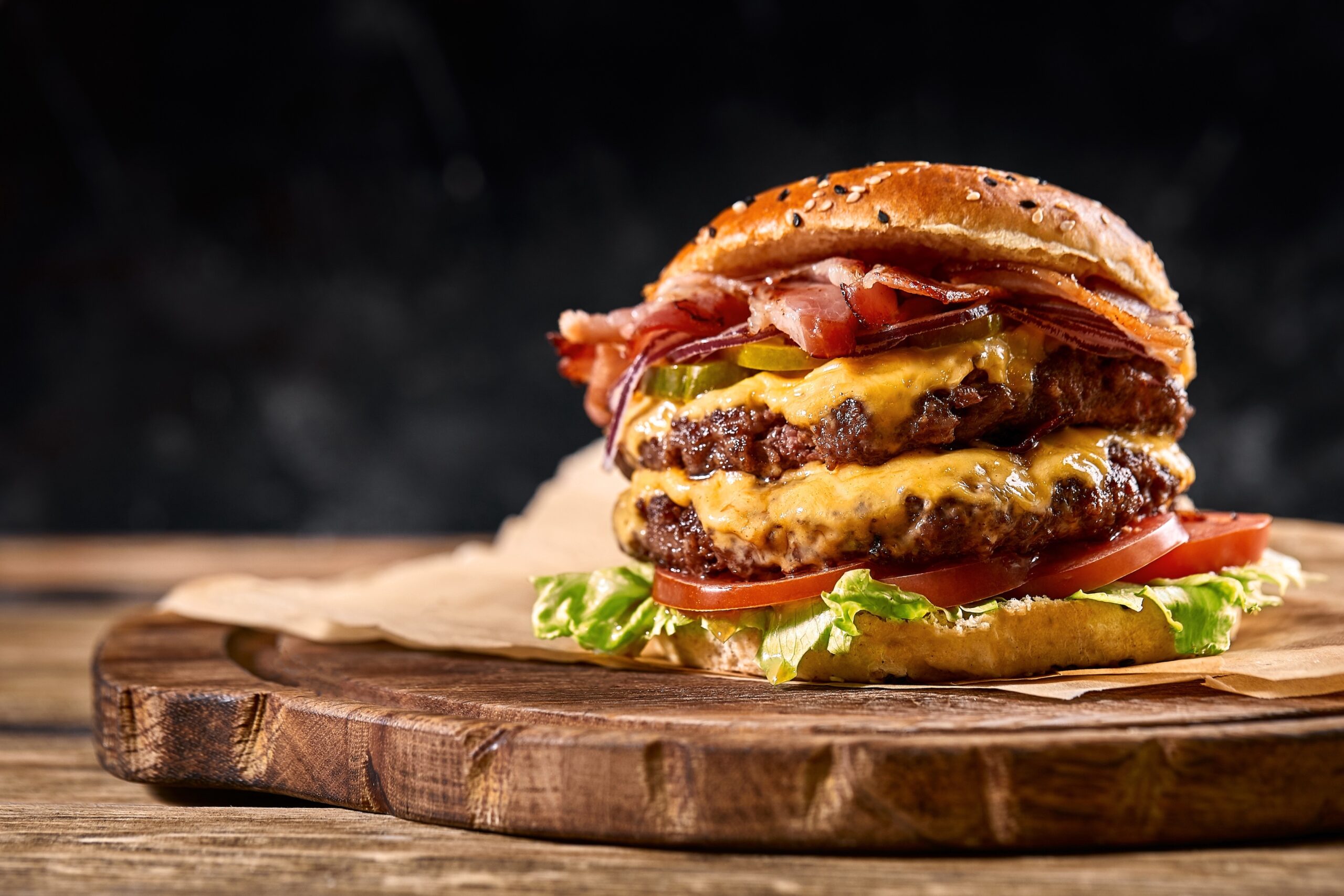 Juicy American burger, hamburger or cheeseburger with two beef patties, with sauce and basked on a black background. Concept of American fast food. Copy space.